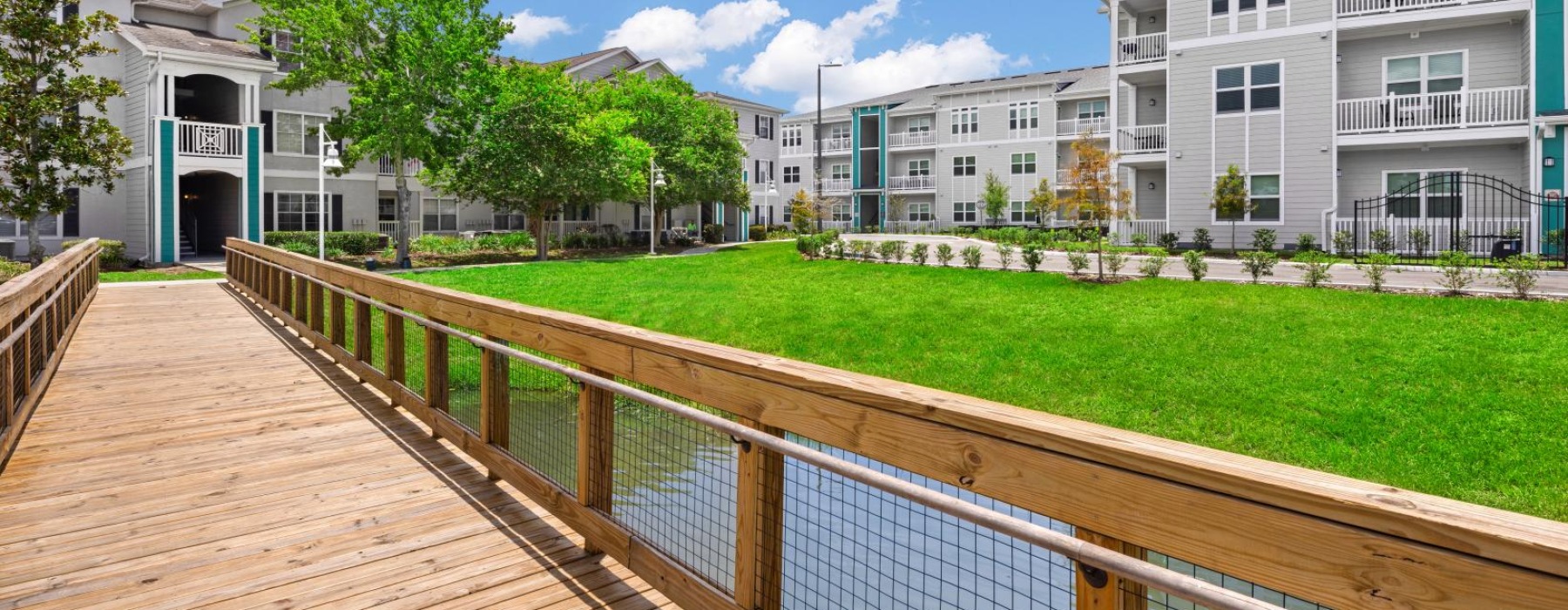a long wooden walkway leading to a building with a grass lawn and trees
