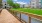 a long wooden walkway leading to a building with a grass lawn and trees